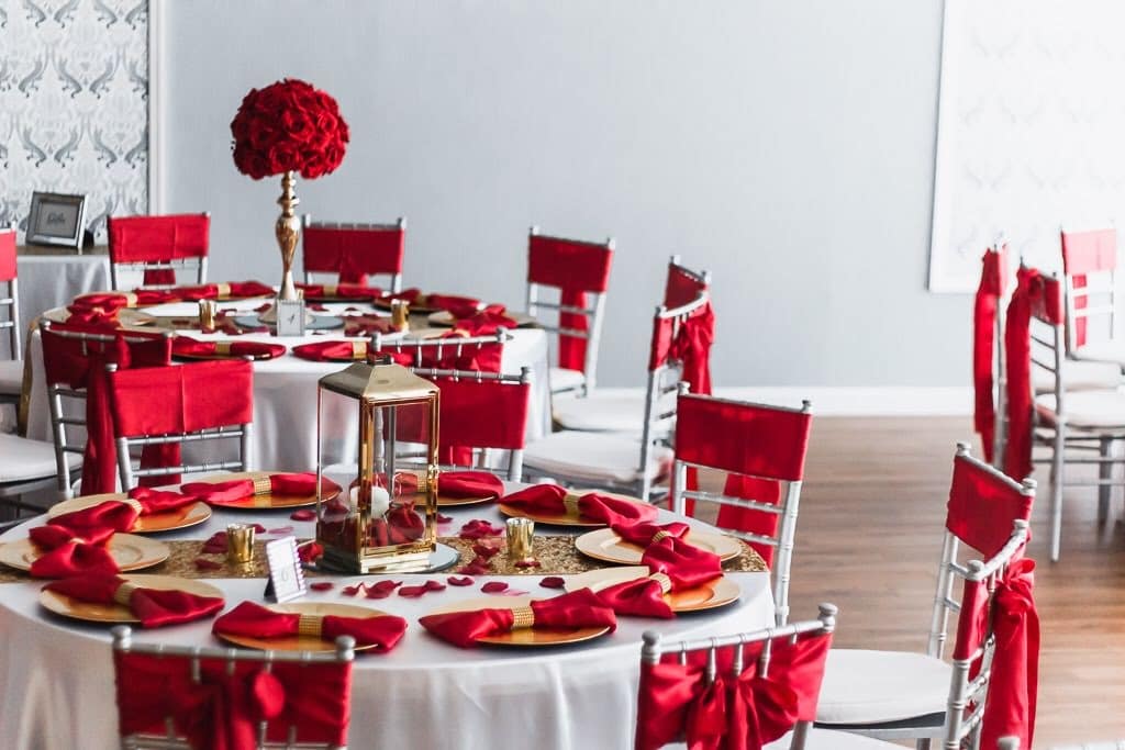 round tables with white table cloths and red accents with tall red floral arrangements in white room
